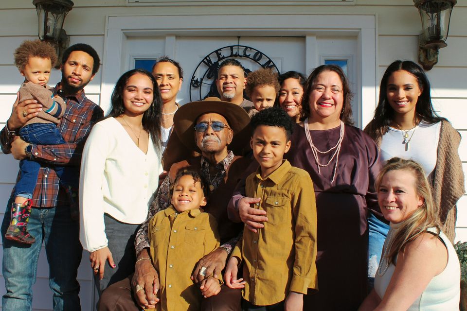 A large multi-generational family gathers on a front porch, from grandparents to toddlers.
